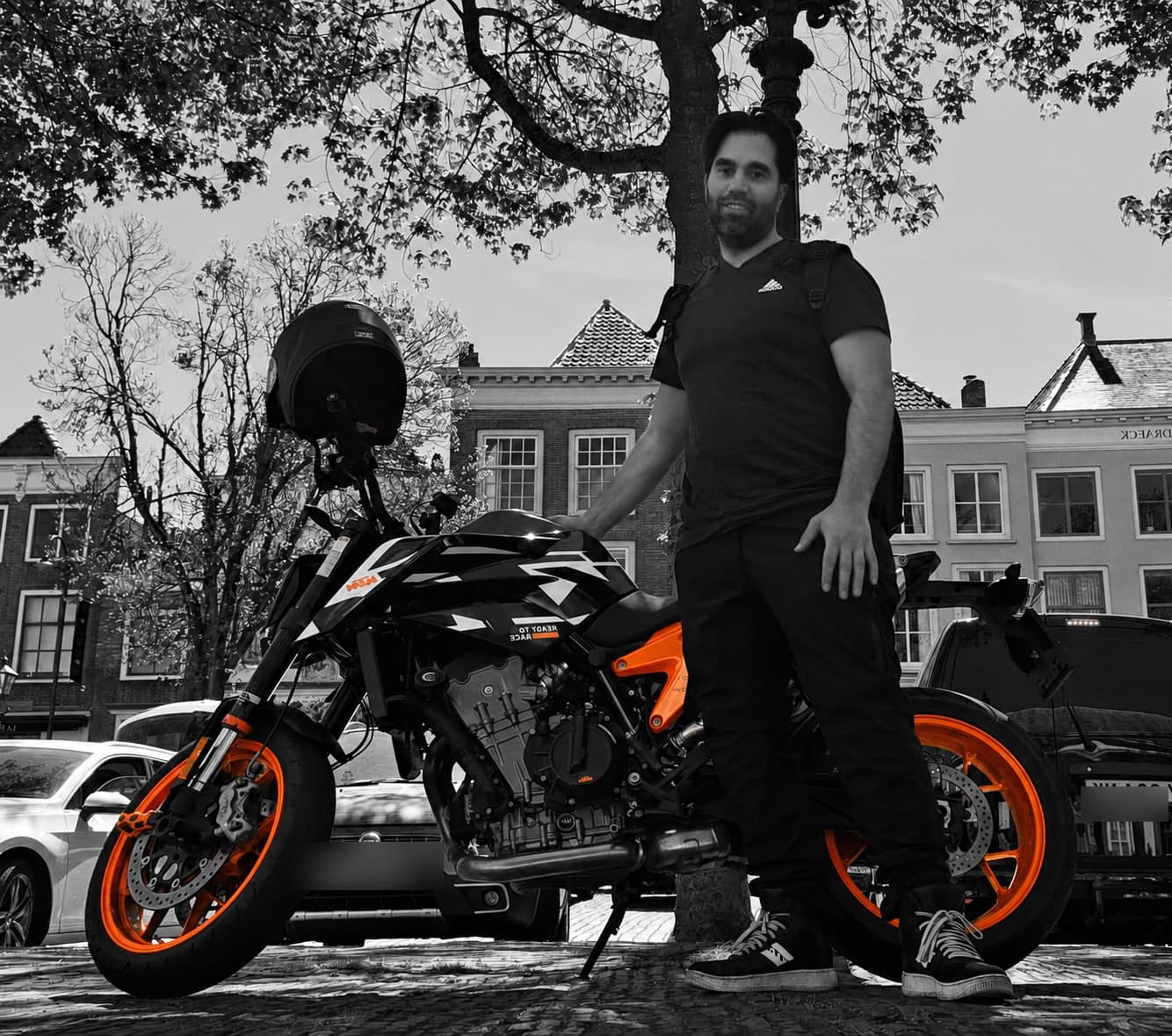 Patrik Zorica standing with his orange-accented KTM motorcycle on a cobbled street